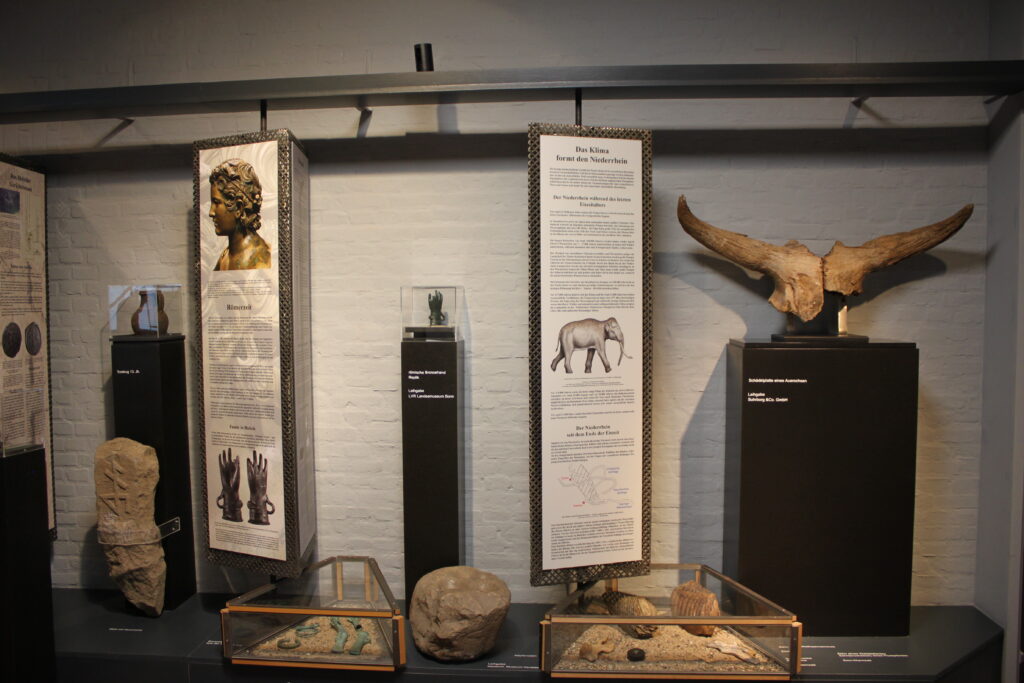 Eine Ausstellungswand mit verschiedenen historischen Objekten, Skulpturen und Informationstafeln.