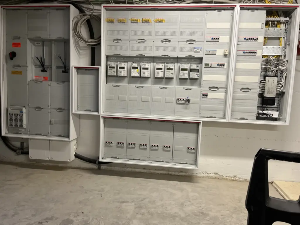 Ein elektrischer Verteiler mit Sicherungen und Zählern an einer Wand in einem Keller.