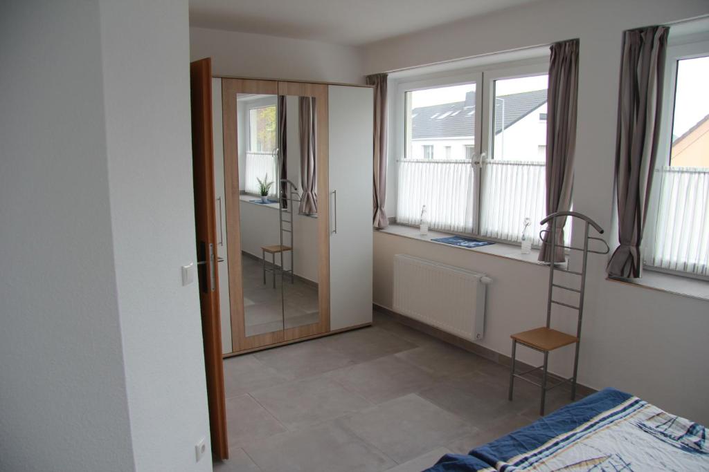 Helles Zimmer mit einem Bett, einem Stuhl, einem Spiegel und Fenster mit Vorhängen.