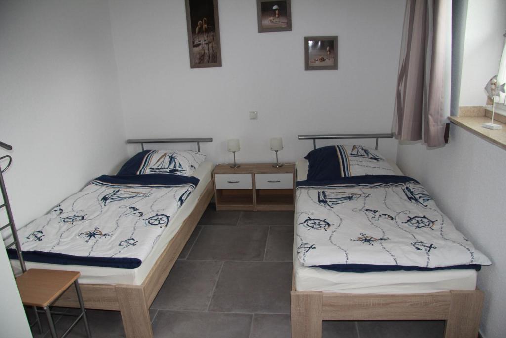 Zwei Einzelbetten mit maritimen Bettbezügen stehen in einem hellen Zimmer mit Fenstern und Bildern an der Wand.