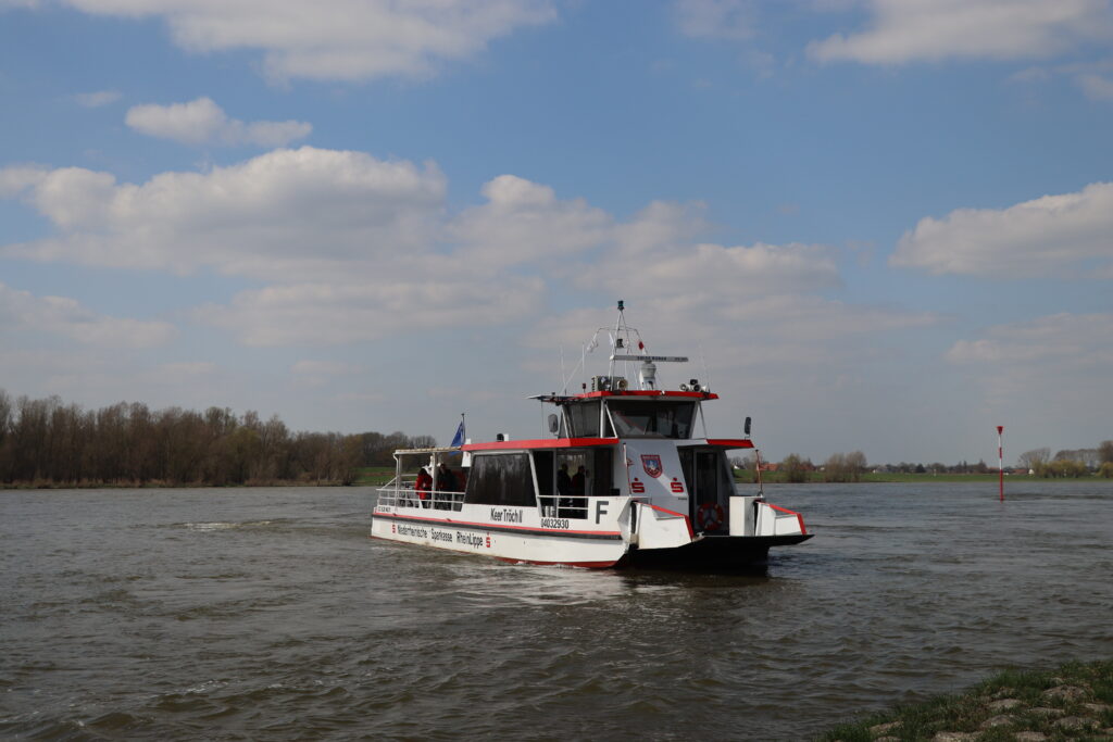 Ein Passagierschiff fährt auf einem Fluss unter einem teilweise bewölkten Himmel.