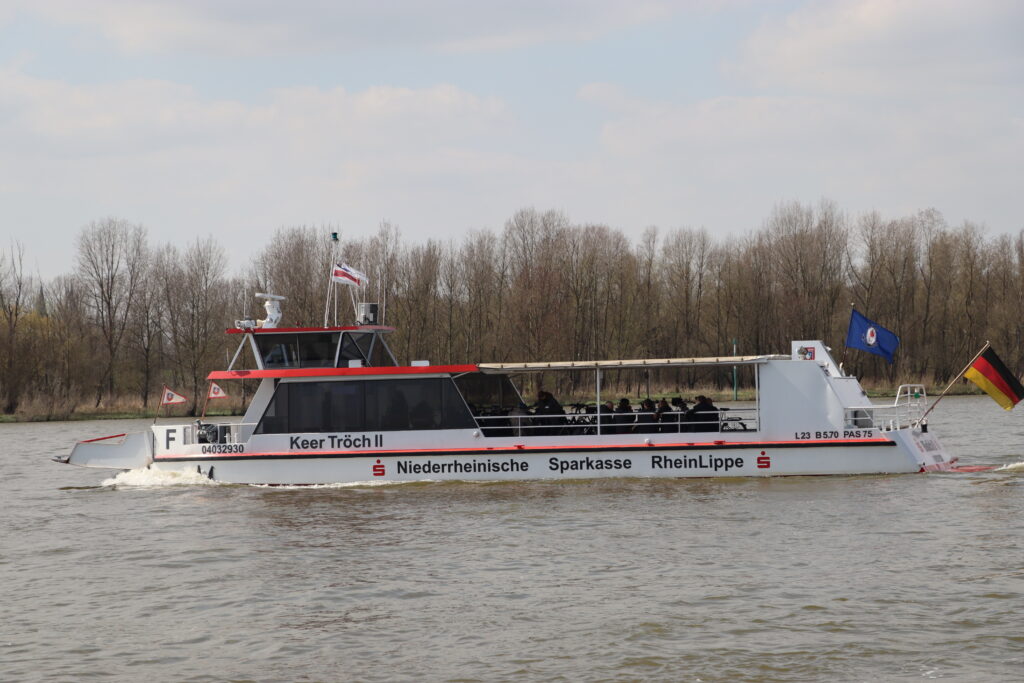 Ein Passagierboot fährt auf dem Wasser, umgeben von Bäumen und unter einem bewölkten Himmel.