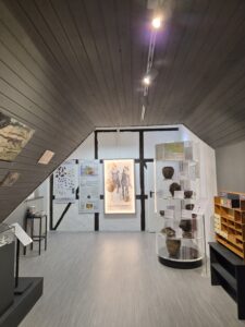 Innenansicht eines Ausstellungsraums mit Vitrinen, Ausstellungsstücken und informativen Tafeln an den Wänden.