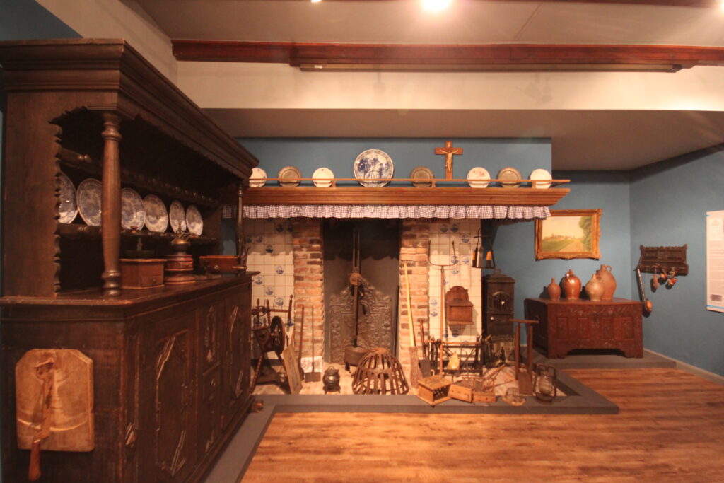 Historisches Dorfmuseum mit einer rustikalen Küche, einem offenen Kamin und antiken Möbeln und Geschirr.