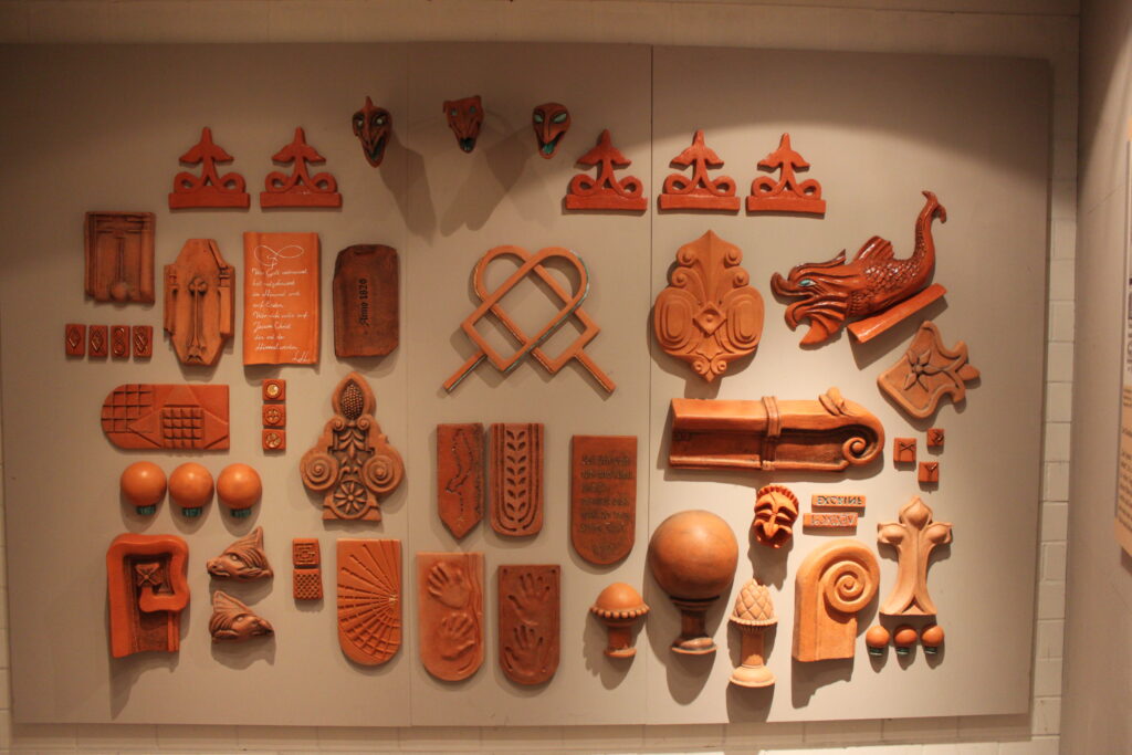 Eine Wand mit verschiedenen terrakottafarbenen Ornamenten und reliefartigen Verzierungen in unterschiedlichen Formen und Größen.