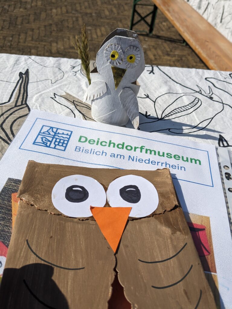 Die Tischdekoration im Deichdorfmuseum zeigt eine Papier-Eule und eine zuvor gefaltete Figur auf einem Tisch.