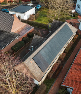 Dachansicht eines Hauses mit Solarpanelen, umgeben von Gärten und anderen Wohnhäusern in einer ländlichen Umgebung.
