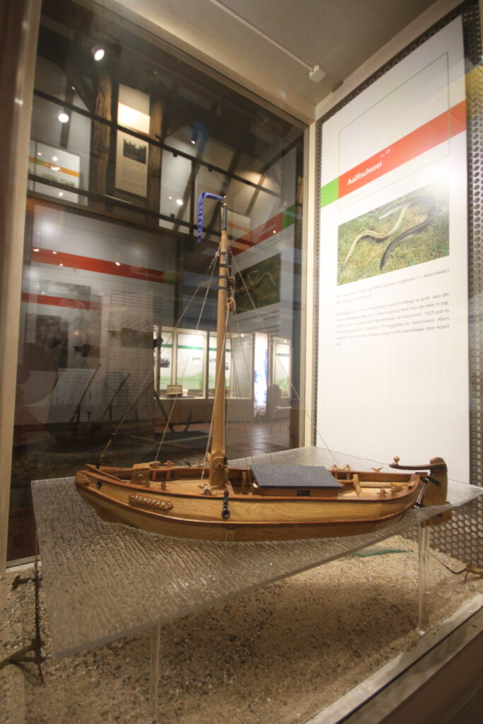 Eine Holzschiffsmodell in einer Glasvitrine, umgeben von informationalen Displays über die Region.