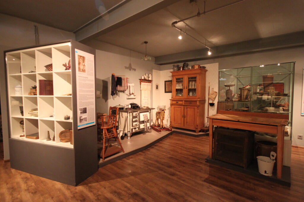Eine Ausstellung mit historischen Möbeln und Werkzeugen in einem Raum mit Holzboden und beleuchteten Vitrinen.