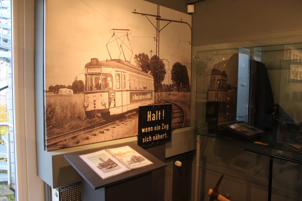Eine historische Fotografie eines Triebwagens an einem Bahnübergang mit vorangehender Warnsignal-Tafel.