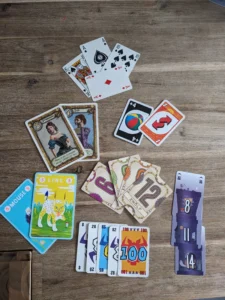 Auf einem Holztisch liegen verschiedene Spielkarten und farbige Spielkarten, darunter Zahlen- und Aktionskarten.