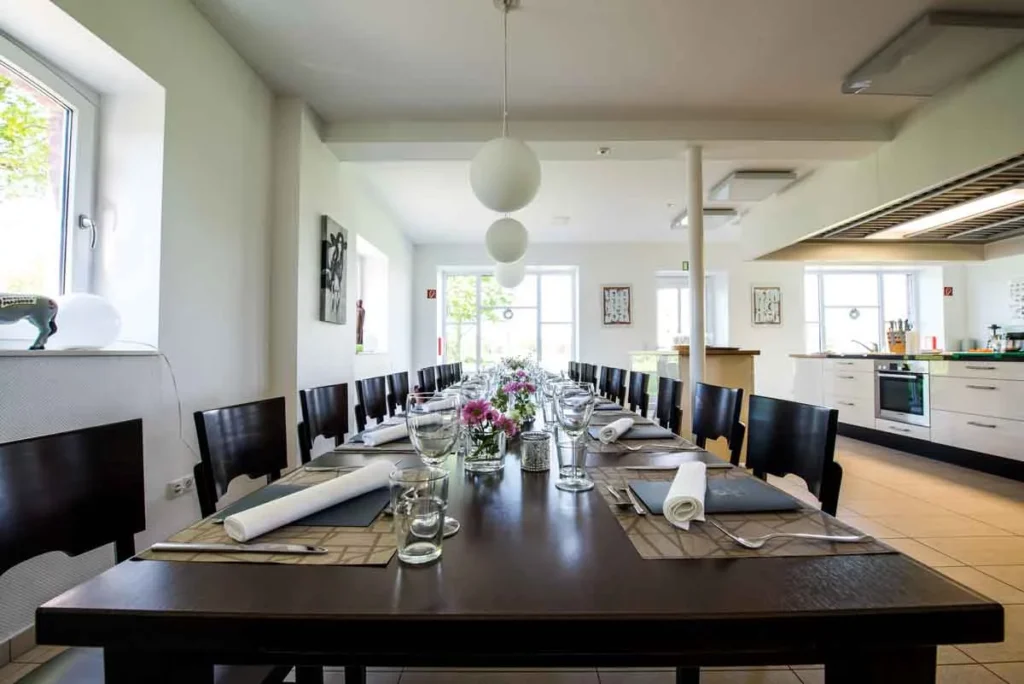 Ein festlich gedeckter Tisch mit Besteck, Gläsern und Blumen in einem hellen Raum mit moderner Küchenausstattung.