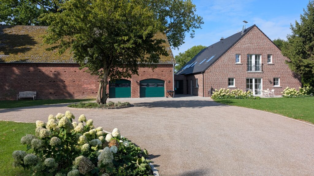 Eine großzügige Hofanlage mit zwei Backsteinhäusern, einer Garage und blühenden Hortensien im Vordergrund.