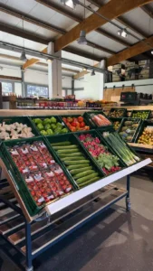 Gemüse- und Obstregale in einem Laden, mit frischen Produkten wie Tomaten, Gurken und Äpfeln in ansprechender Anordnung.