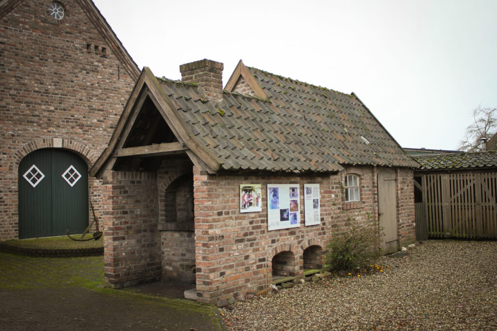Ein kleiner, historischer Ziegelbau mit einem Satteldach und Bildern an der Wand steht in einem steinigen Umfeld.