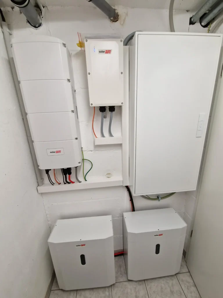 In einem Nebenraum sind zwei weiße Batteriespeicher und ein Steuerungssystem an einer Wand installiert.