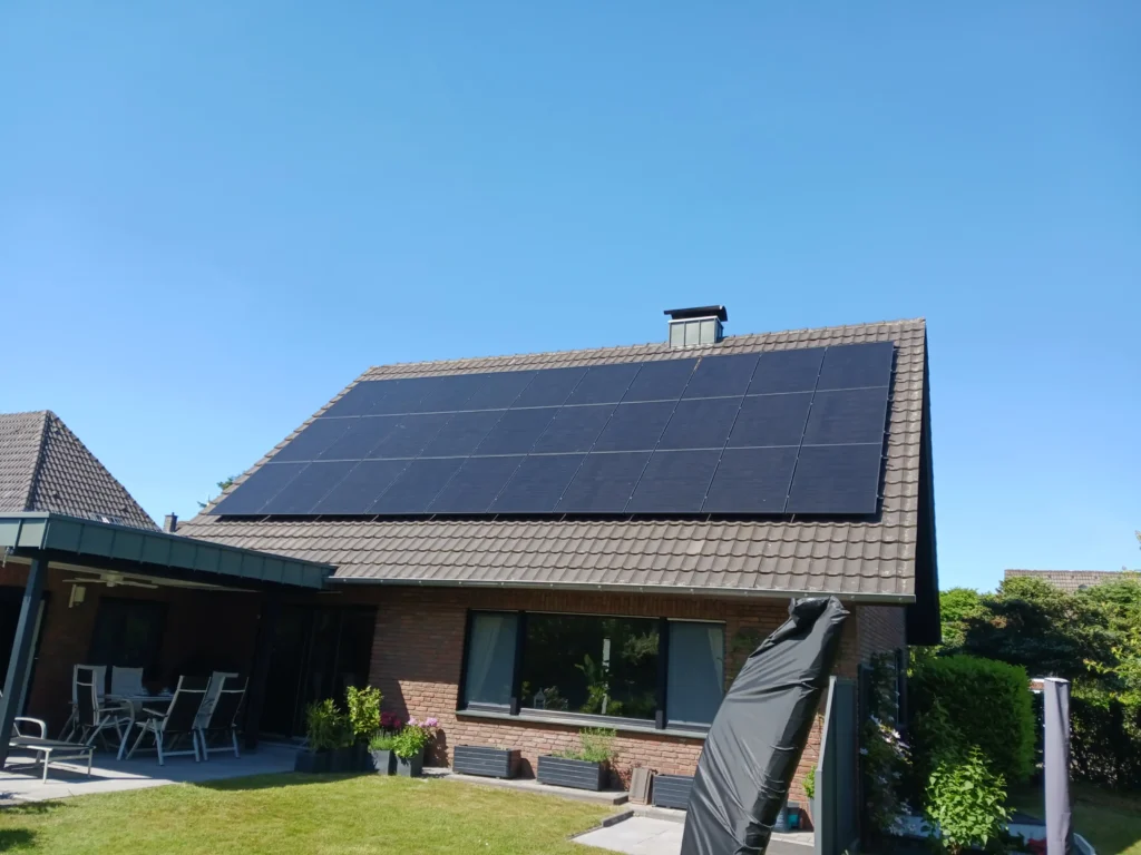 Ein Wohnhaus mit einem Dach voller Solarpaneele unter klarem blauen Himmel und einem gepflegten Garten im Vordergrund.