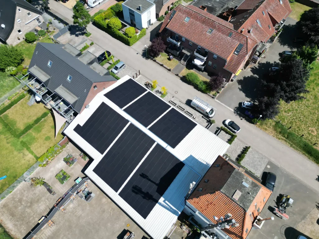 Dächer zweier Wohnhäuser mit installierten Solarpanels, umgeben von grünen Gärten und Straßen im Dorf.