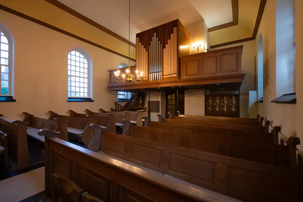Eine Innenansicht einer Kirche mit Holzbänken und einer Orgel im oberen Bereich.