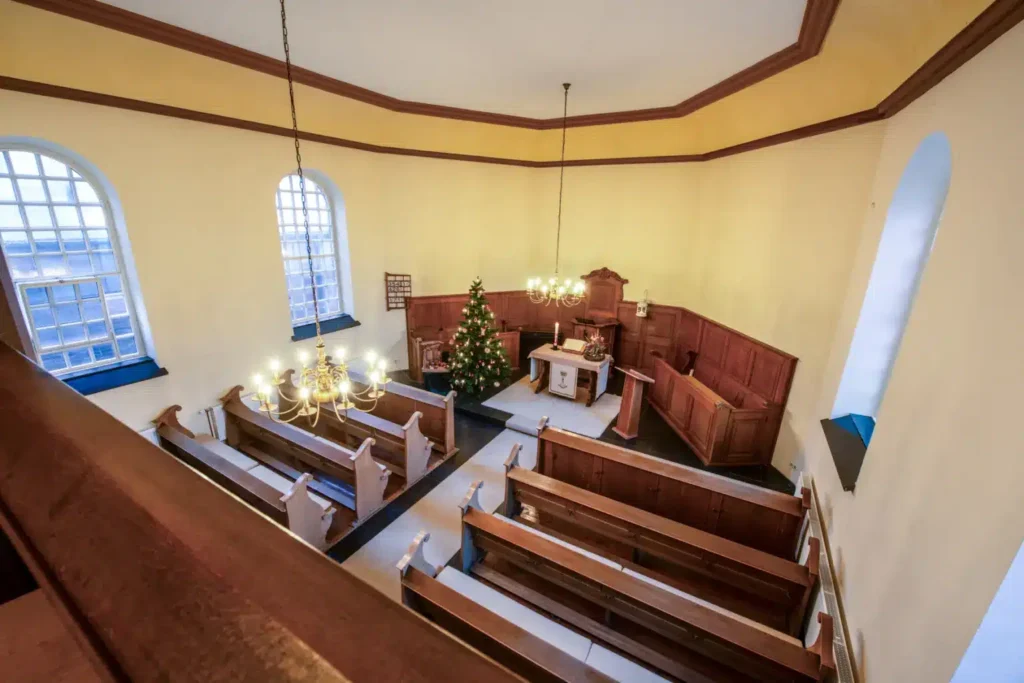 Der Innenraum einer Kirche mit Weihnachtsbaum, Bänken und geschmücktem Altar, beleuchtet von Kronleuchtern.