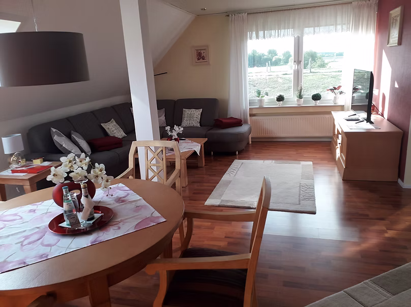 Ein runder Esstisch mit Stühlen. Dahinter das offene Wohnzimmer mit grauer Couch.