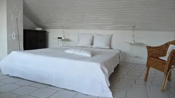 Helles, minimalistisches Schlafzimmer mit Doppelbett, einem Stuhl und dekorativen Elementen an Wänden und Fenster.