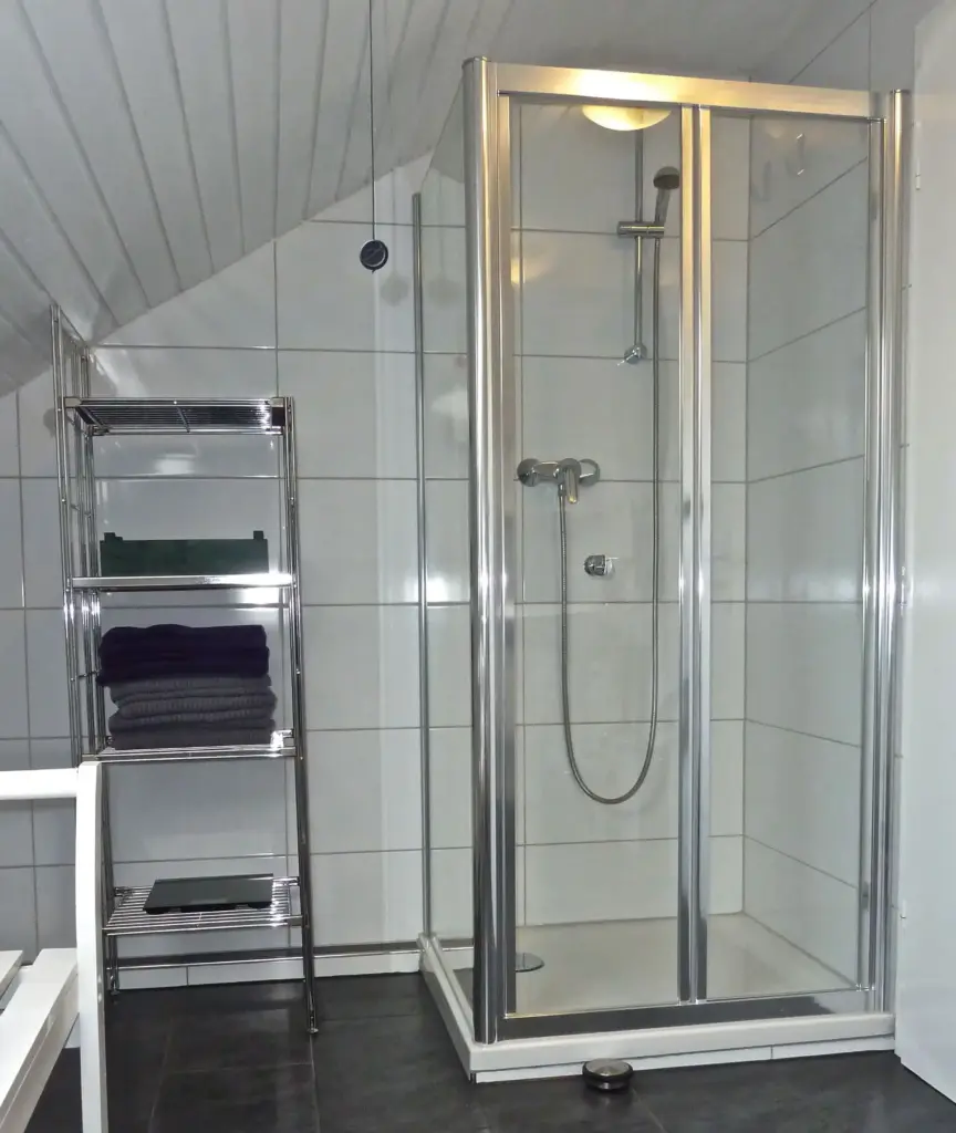 Modern ausgestattete Duschkabine mit gläserner Abtrennung und Handtuchablage in einem Badezimmer.