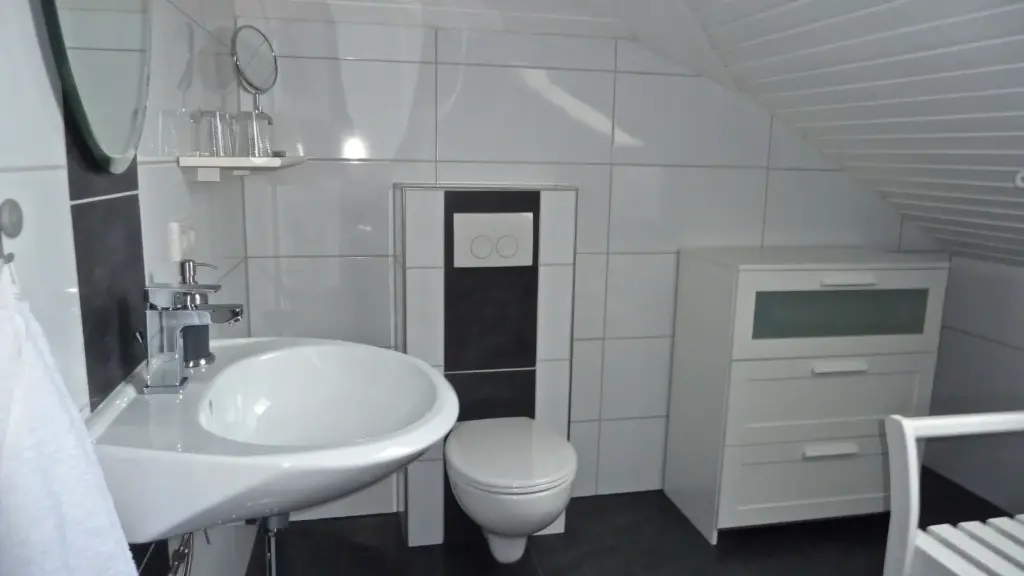 Helles Badezimmer mit Waschtisch, Toilette, einem weißen Schrank und einer Wand mit großen, hellen Fliesen.
