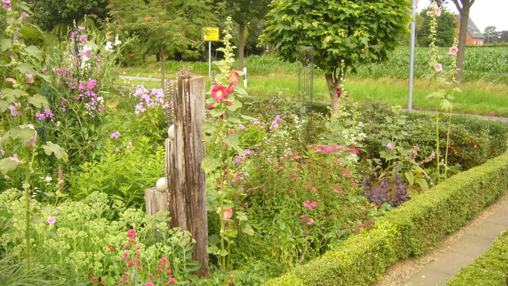Eine blühende Gartenlandschaft mit verschiedenen Blumen, Sträuchern und einem Holzelement im Vordergrund.