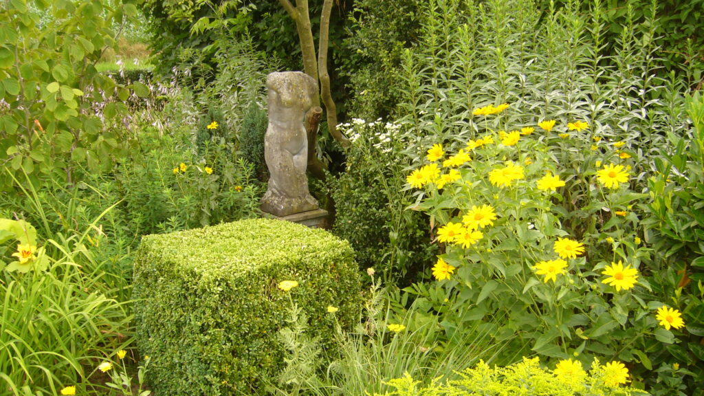 Eine Skulptur im Garten umgeben von bunten Blumen und üppigem Grün.