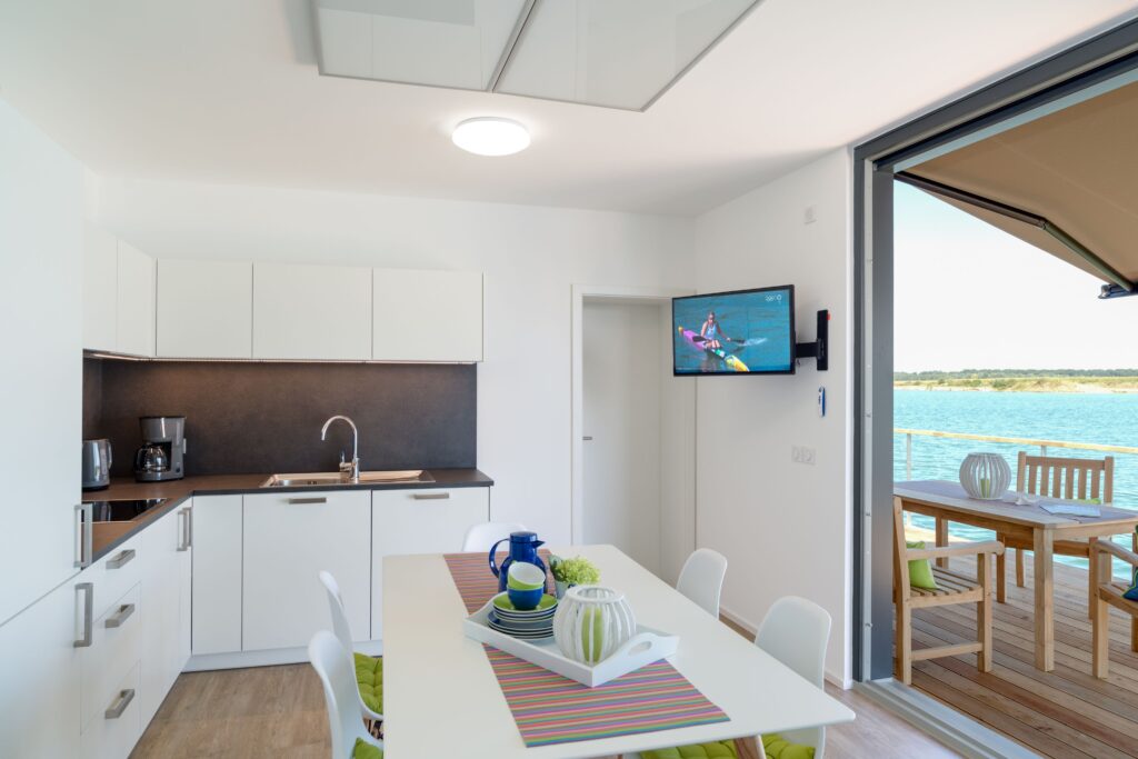 Helle, moderne Küche mit Essbereich und Blick auf den Wasserzugang durch große Fenster.