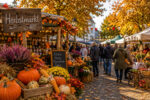 Bunte Stände mit Kürbissen, Blumen und herbstlichen Dekorationen auf einem belebten Markt mit Menschen und buntem Laub.