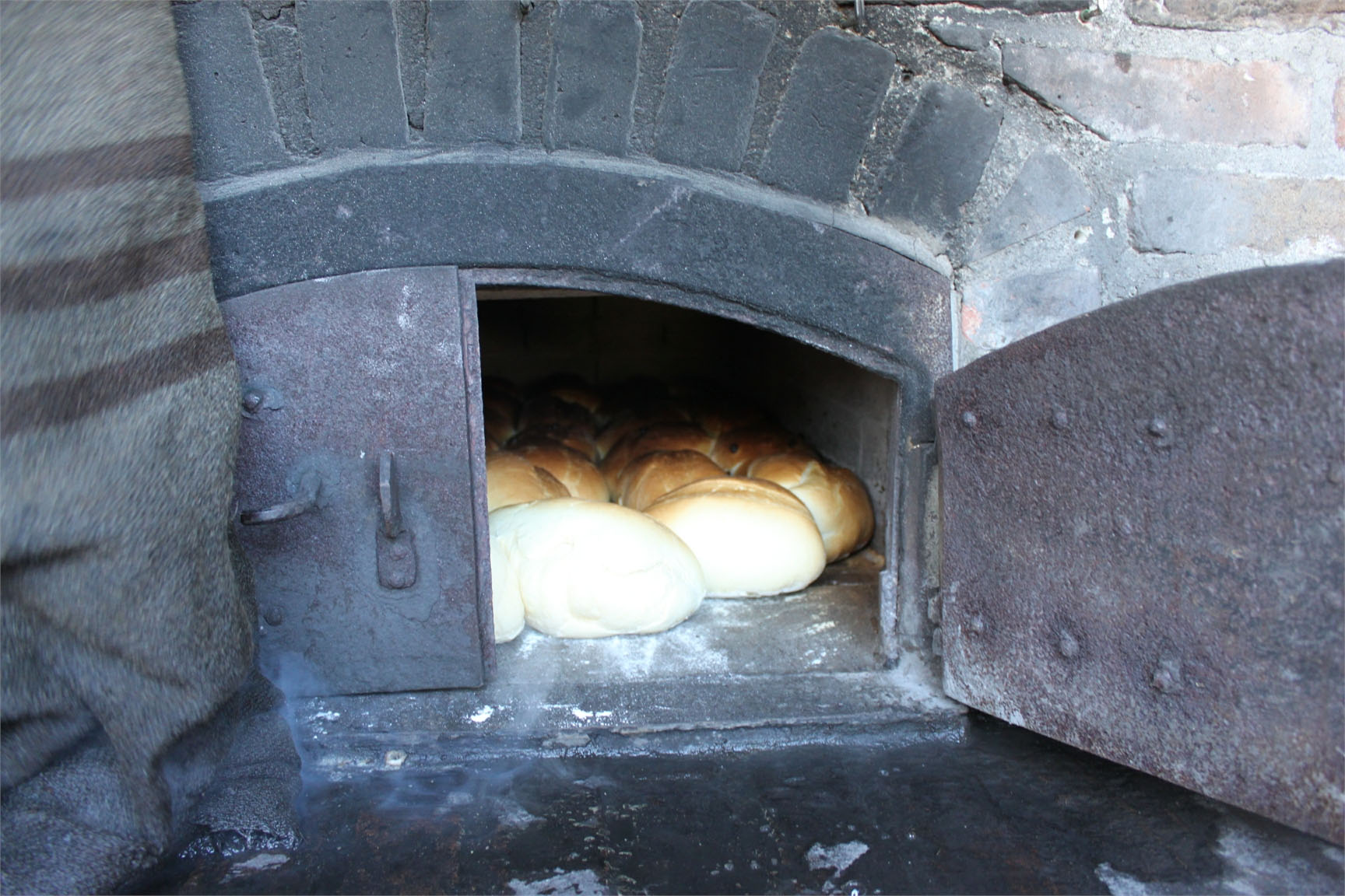 Frisch gebackenes Brot liegt in einem traditionellen Holzofen mit offenem Tor.
