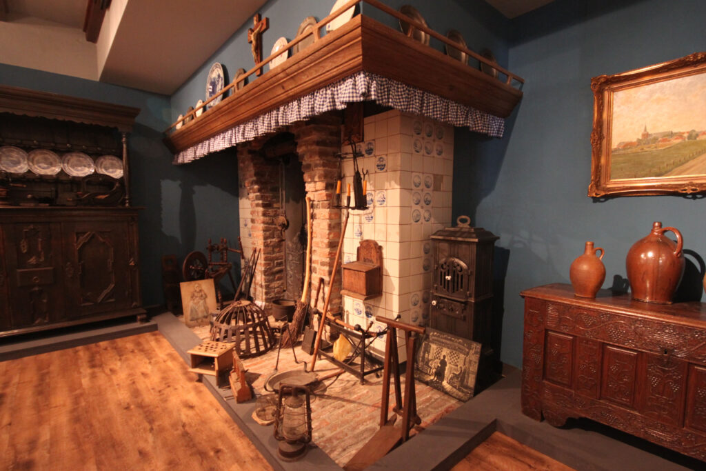 Rustikale Kücheneinrichtung mit einem großen Kamin, Holzregalen und historischen Haushaltsgegenständen in einem Raum.