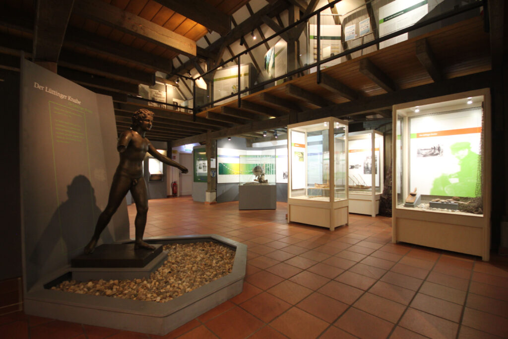 Im Ausstellungsraum stehen Vitrinen mit historischen Exponaten und einer Statue auf einem Sockel in der Mitte.