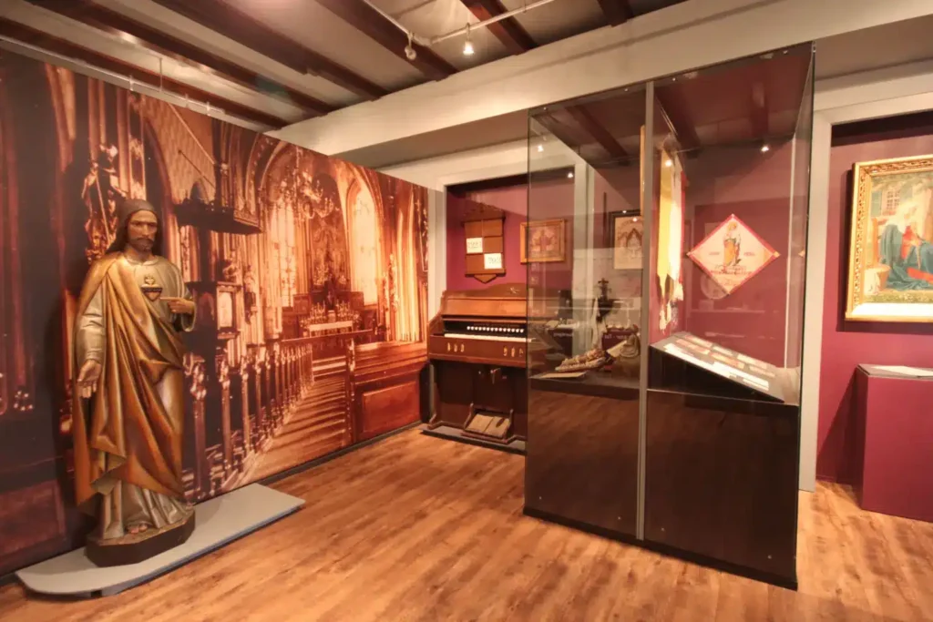 Ein Ausstellungsraum mit einer Statue, historischen Kunstwerken und einer Orgel, die an eine Kirche erinnert.