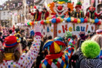 Bunte Karnevalsparade mit Clowns und feierndem Publikum in festlicher Stimmung und Konfetti.