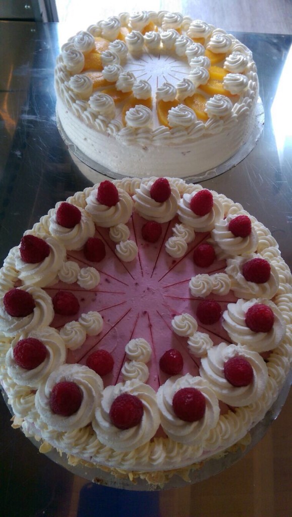 Zwei beeindruckende Torten, eine mit Obst und die andere mit Himbeeren, dekoriert mit Sahnehauben.