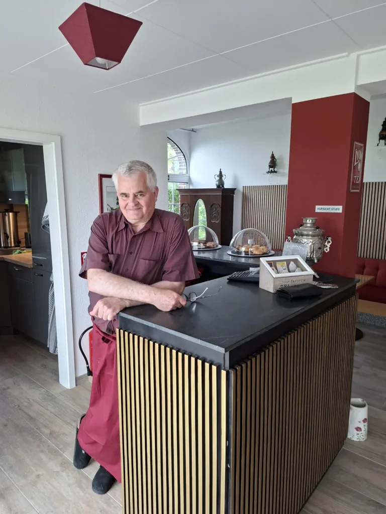Ein älterer Mann steht am Empfangstresen eines einladenden Gasthauses mit warmem Ambiente.