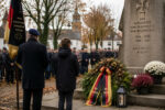 Menschen stehen in einer Gedenkveranstaltung vor einem Kriegerdenkmal, um die Gefallenen der Weltkriege zu ehren.