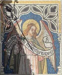Mosaik eines Engels mit einem Banner, umgeben von ornamentalen Mustern in blauen und goldenen Farben.